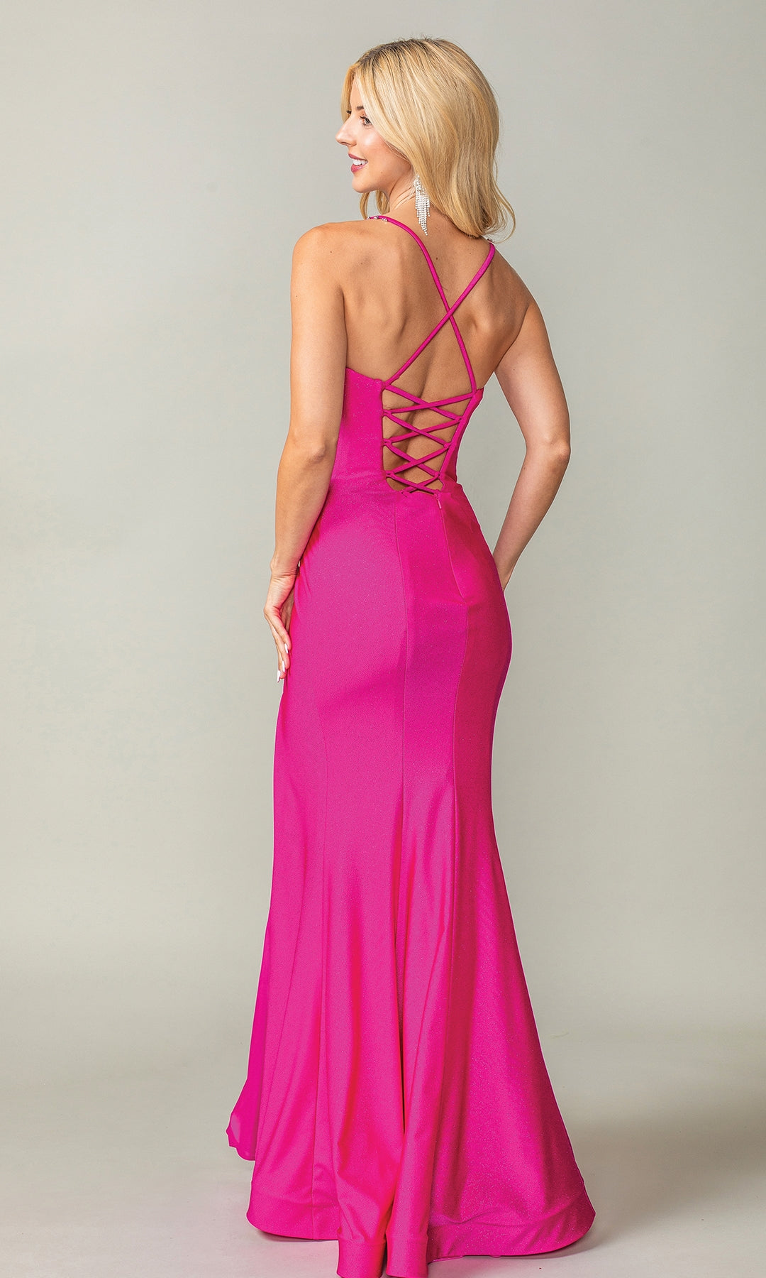 A woman stands with her back to the camera in the Long Prom Dress 4409 by Dancing Queen, a floor-length bright pink fitted gown featuring a lace-up open back.